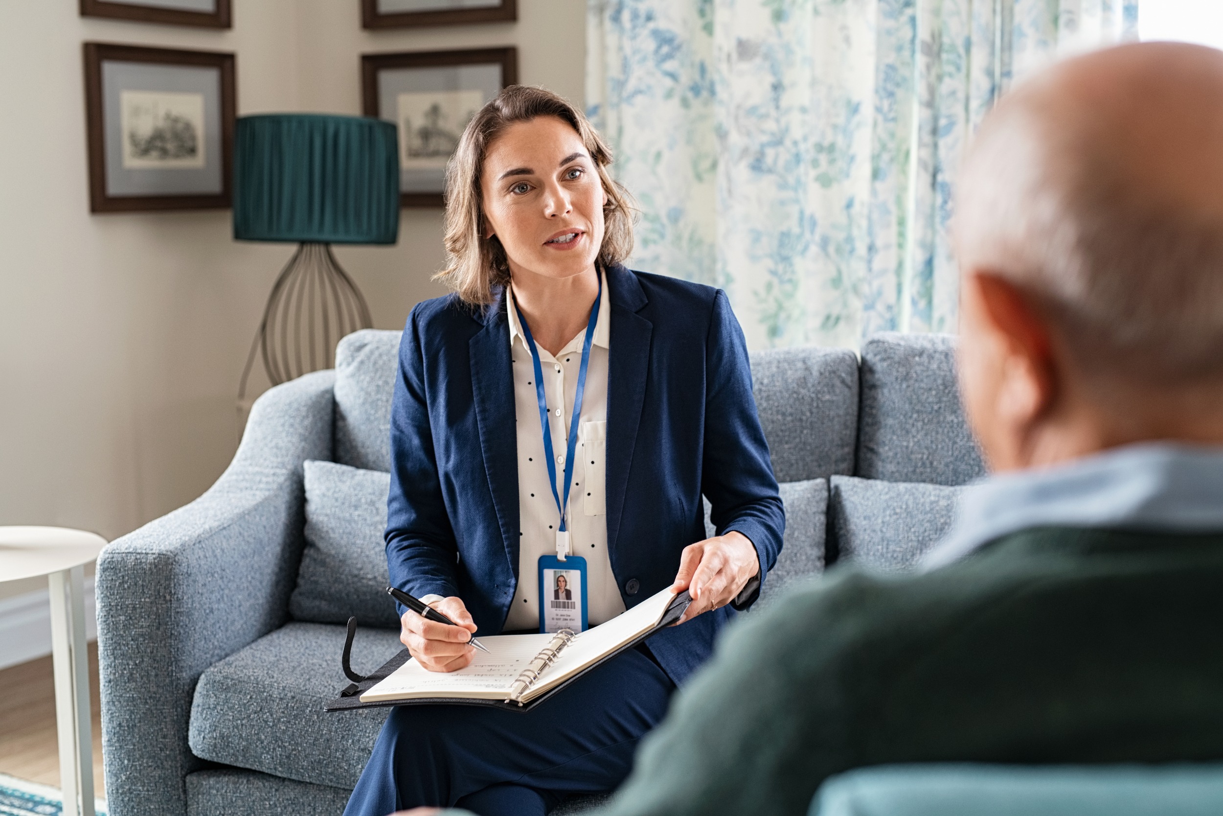 Mature social worker talking to senior man and taking notes of health progress.
