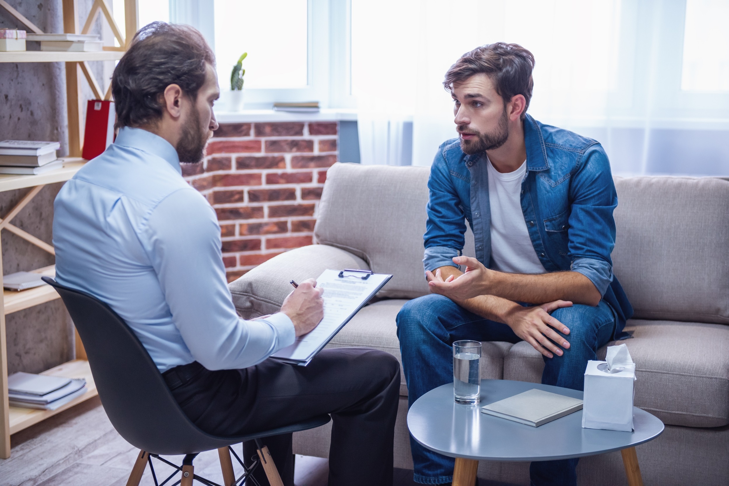 Handsome young man is sitting on couch and talking to the psychologist while